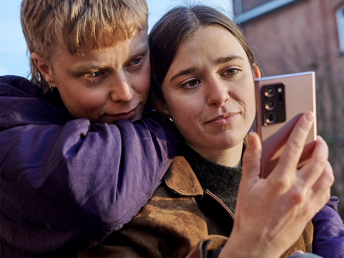 Zwei Personen sehen auf ein Smartphone. Das bild zeigt nur die Gesichter und eine Hand der Personen.
