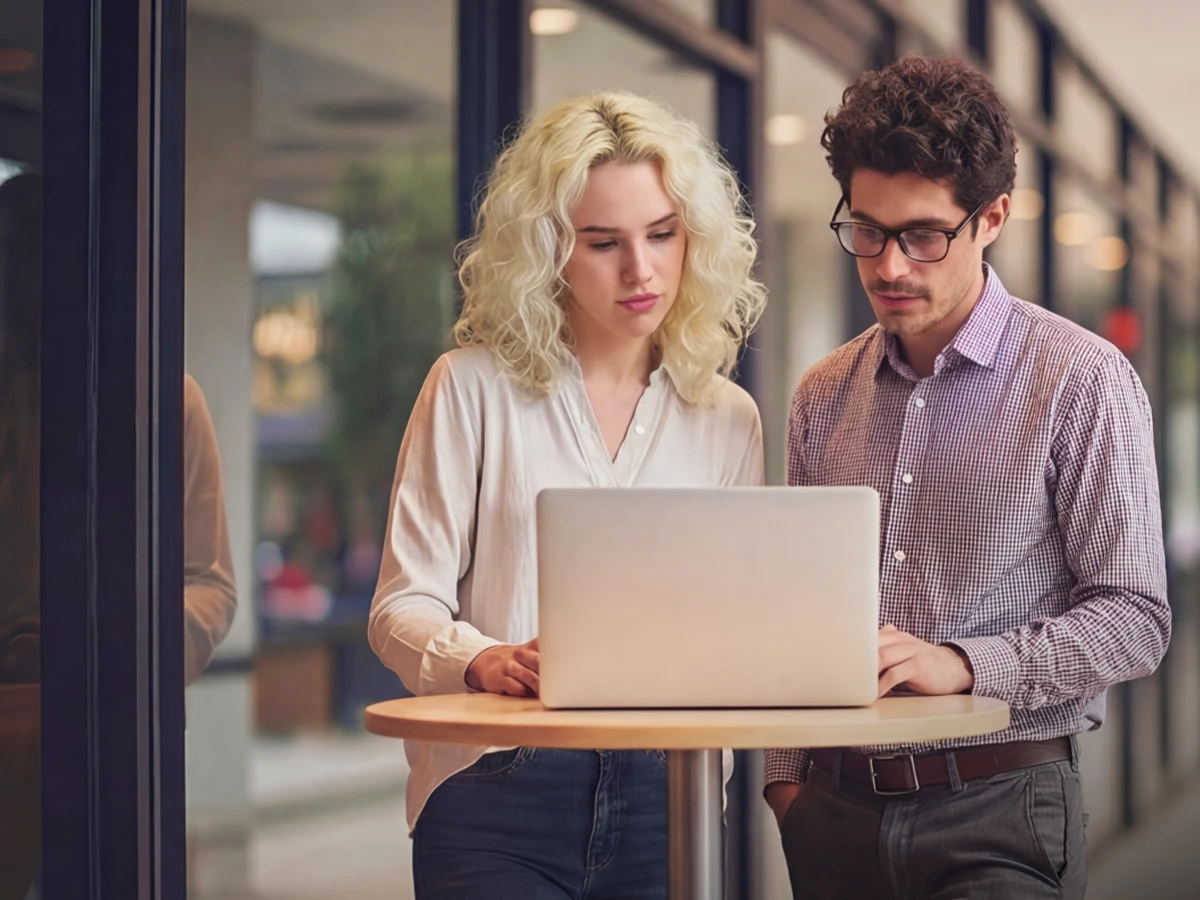 Eine Frau und ein Mann stehen an einem Tisch und schauen in ein Notebook (Header Photo)