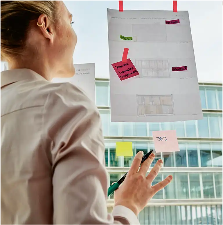 Zwei Personen stehen vor einem Fenster, auf dem verschiedene Post-its kleben (Foto)